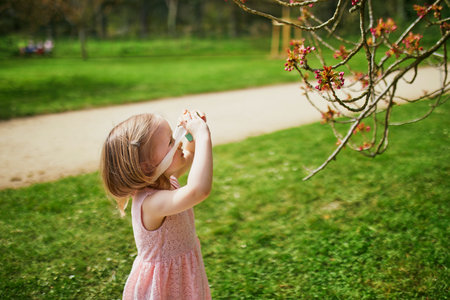 Adorable three year old girl in pink dress enjoying sunny spring day and playing with wooden photo camera in Park of Sceaux near Paris, Franceの写真素材