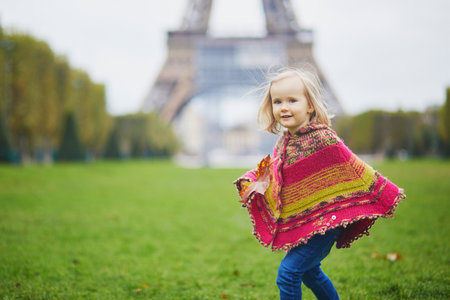 Adorable toddler girl near the Eiffel tower on a fall day in Paris, France. Child enjoying autumn outdoors. Stylish and comfortable autumn clothes for kidsの写真素材