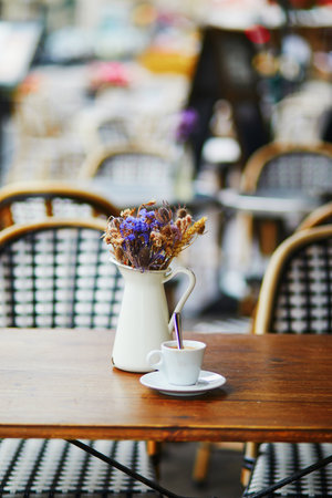 Table of traditional Parisian outdoor cafe. Cup of coffee and pitcher with dried flowers in empty restaurant in Paris, Franceの写真素材