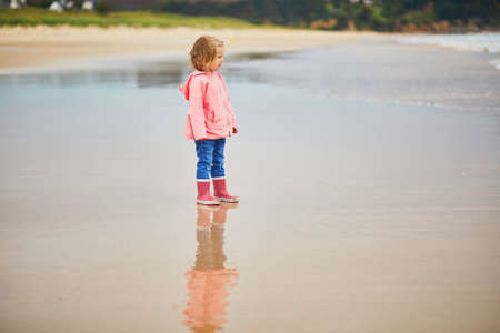 Adorable toddler girl on the sand beach at Atlantic coast of Brittany, France. Small child enjoying vacation by the sea or ocean. Travelling with kidsの写真素材
