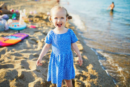 Happy little girl in blue dress having fun on the beach at Mediterranean sea in France. Cheerful kid enjoying vacation at the sea. Outdoor summer activities for childrenの写真素材