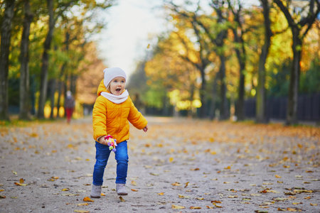 Adorable little girl in yellow jacket walking in autumn park on a sunny fall day. Happy child having...