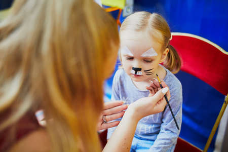 Children face painting. Artist painting little preschooler girl like cat. Creative activities for...