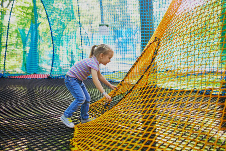 Adorable little girl having fun in adventure park. Child on tree top net trampoline. Outdoor activities for small kidsの写真素材