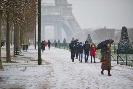 PARIS, FRANCE - JANUARY 16, 2021: People passing by the Eiffel tower in Paris on a day with heavy snow. Unusual weather conditions in Paris, Franceのeditorial素材
