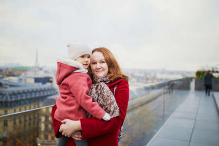 Young woman holding adorable todler girl while enjoying the view from Parisian rooftop terrace. Mothe and daughter in Paris, Franceの写真素材