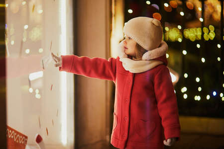 Toddler girl looking at window glass of large department store decorated for Christmas. Child enjoying holiday season in Paris, Franceの写真素材