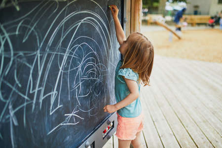 Adorable toddler girl drawing with chalks on easel. Outdoor activity and creative games for small kidsの写真素材