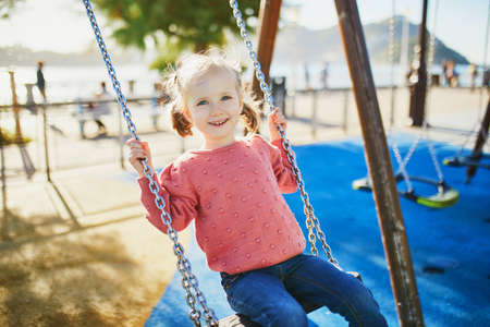 Happy 4 years old girl on a swing. Happy kid on playground swinging on seesaw. Outdoor summer activities for childrenの写真素材