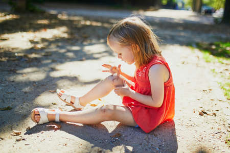 Cute little girl sitting on the ground after falling down. Child getting hurt while walking in park....