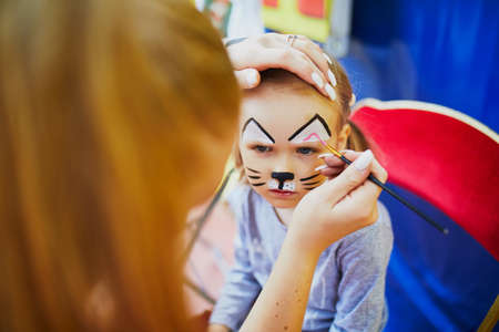 Children face painting. Artist painting little preschooler girl like cat. Creative activities for kidsの写真素材