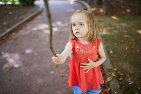 Adorable preschooler girl playing with a stick on a sunny street. Outdoor summer activities for kids. Active games for childrenの写真素材