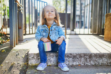 Adorable 4 year old girl drawing with colorful chalks on asphalt. Outdoor activities for kids
