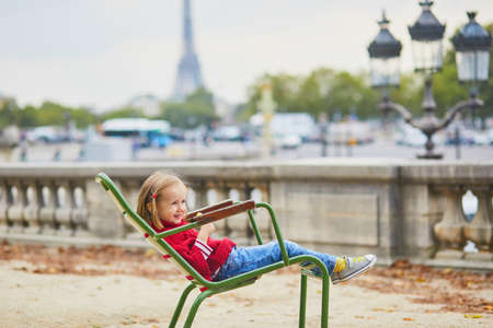 Adorable preschooler girl sitting on green chair in Tuileries garden in Paris, on a fall day. Happy child enjoying autumn day. Fall season in France. Outdoor autumn activities for kidsの写真素材