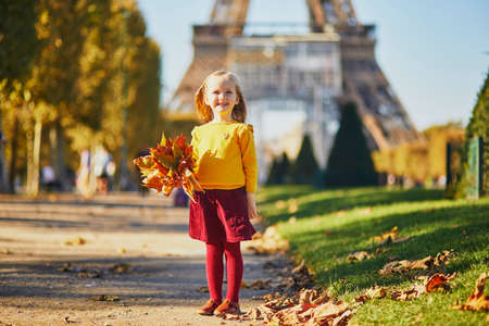 Adorable preschooler girl enjoying nice and sunny autumn day outdoors. Happy child gathering autumn leaves near the Eiffel tower in Paris, France. Outdoor fall activities for kidsの写真素材