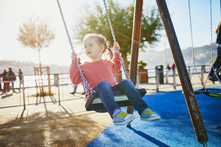 Happy 4 years old girl on a swing. Happy kid on playground swinging on seesaw. Outdoor summer activities for childrenの写真素材