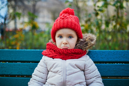 Sad preschooler girl sitting on the bench on a street of Paris, France