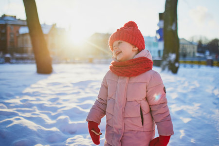 Adorable preschooler girl having fun in beautiful winter park on a snowy cold winter day. Cute child playing in snow. Winter activities for family with kidsの写真素材