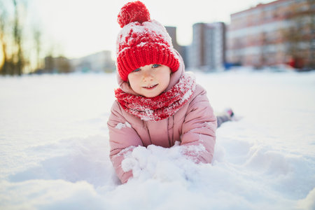 Adorable preschooler girl having fun in beautiful winter park on a snowy cold winter day. Cute child playing in snow. Winter activities for family with kidsの写真素材