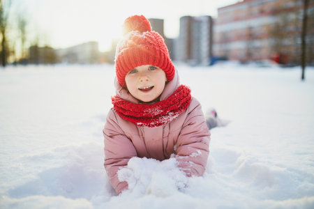 Adorable preschooler girl having fun in beautiful winter park on a snowy cold winter day. Cute child...