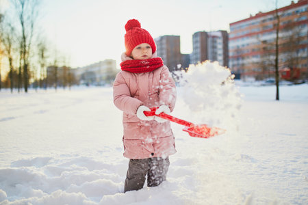 Adorable preschooler girl having fun in beautiful winter park on a snowy cold winter day. Cute child playing in snow. Winter activities for family with kidsの写真素材