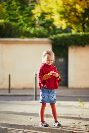 Adorable preschooler girl having fun on a street on a fall day. Outdoor autumn activities for kidsの写真素材