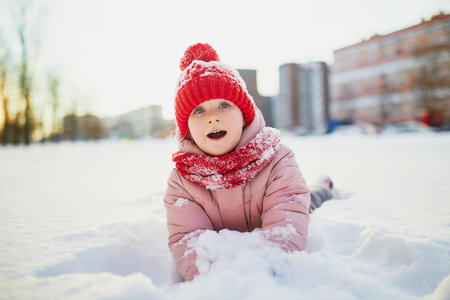 Adorable preschooler girl having fun in beautiful winter park on a snowy cold winter day. Cute child playing in snow. Winter activities for family with kidsの写真素材