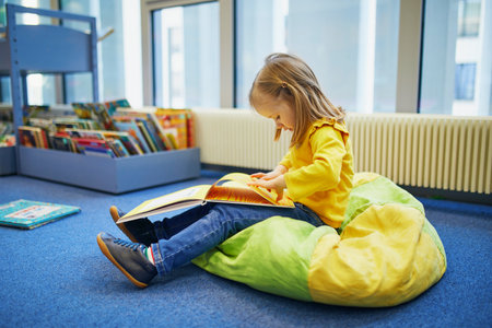 4 year old girl sitting on the floor in municipal library and reading a book. Reading and learning...