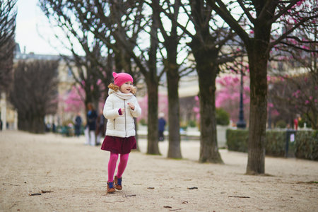 Cheerful preschooler girl having fun on a street of Paris, France in the beginning of spring with pink magnolias in bloomの写真素材