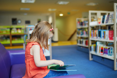 Preschooler 4 year old girl reading a book in municipal libraryの写真素材
