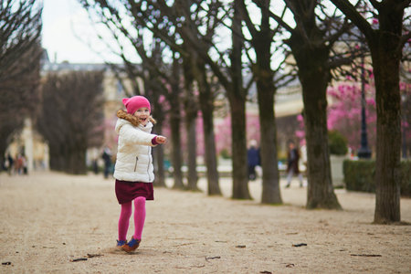 Cheerful preschooler girl having fun on a street of Paris, France in the beginning of spring with pink magnolias in bloomの写真素材