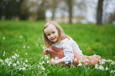 Cute preschooler girl in pink tutu skirt sitting in the grass with many snowdrop flowers in park or forest on a spring day. Little kid exploring nature. Outdoor activities for childrenの写真素材