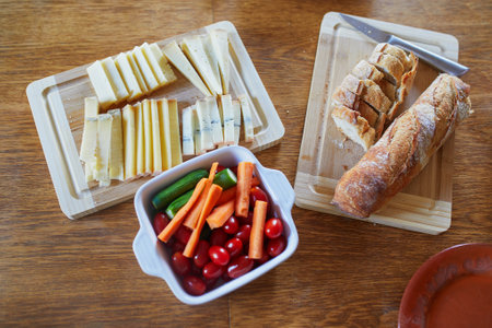 Various types of cheese, vegetables and fresh white bread on the wooden tableの写真素材