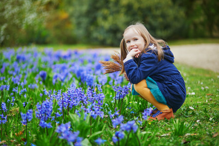 Adorable preschooler girl enjoying nice spring day in park during hyacinth blooming season. Outdoor springtime activities for kids. Little child exploring natureの写真素材