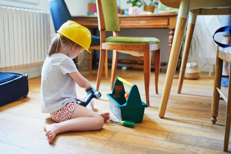 Adorable preschooler girl playing with repair tools at home. Indoors activities for kidsの写真素材