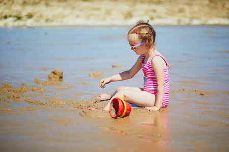 Preschooler girl playing on the sand beach at Atlantic coast of Normandy, France. Outdoor summer activities for kidsの写真素材