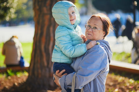 Senior woman holding preschooler girl in her arms on the street. Grandmother and granddaughter walking together in Istanbul, Turkey. Travelling with kids conceptの写真素材