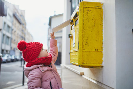Adorable preschooler girl putting letter in yellow post box on a street of Paris, Franceの写真素材