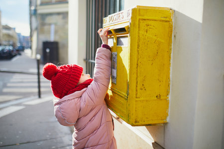 Adorable preschooler girl putting letter in yellow post box on a street of Paris, Franceの写真素材