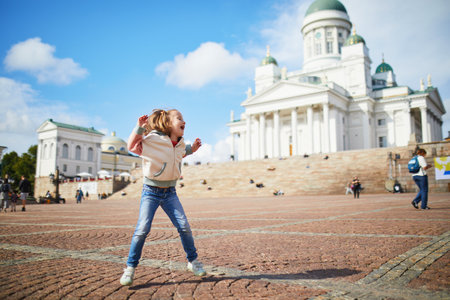 Adorable preschooler girl jumping near Helsinki Cathedral (Helsingin tuomiokirkko) on Senaatintori in Helsinki, Finland. Travelling with kids conceptの写真素材