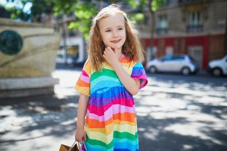 Cute preschooler girl in in rainbow dress on a street of Paris on a summer day