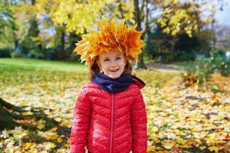 Adorable preschooler girl in maple leaves head decoration enjoying nice and sunny autumn day outdoors. Happy child walking on a fall day in Paris, Franceの写真素材