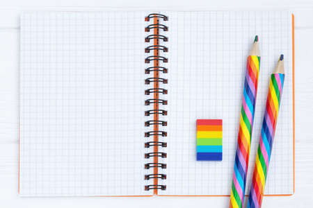 Open copybook with two rainbow-coloured pencils and a rubber on white wooden tableの写真素材