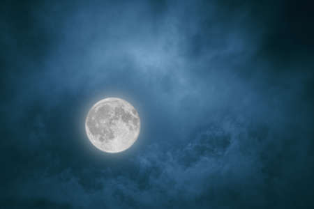 Full moon in the night sky shining through the cloudsの写真素材