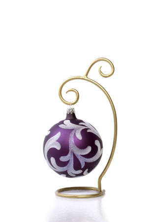 A pretty purple Christmas ball ornament hanging on a gold ornament hanger against a bright white background with a mild reflection/shadow beneath with plenty of copy space.の写真素材