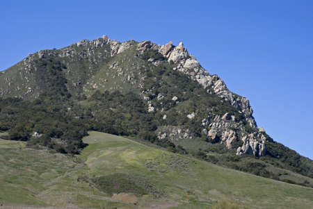 A green, rolling hillside with massive rock outcroppings against a bright, blue sky の写真素材