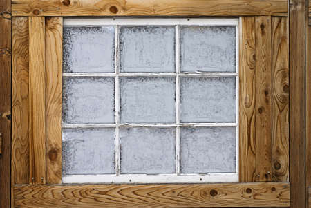 Horizontal image of an old wooden nine-lite window pane in a wooden wall, covered in ice crystals の写真素材