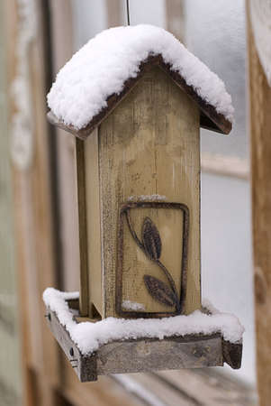 A hanging wooden birdfeeder sits empty beneath a mantle of winter snow の写真素材