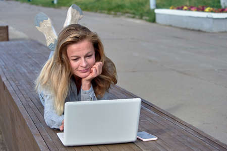A woman with a laptop sits on a wooden platform, works onlineの写真素材
