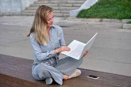 A woman with a laptop sits on a wooden platform, works online